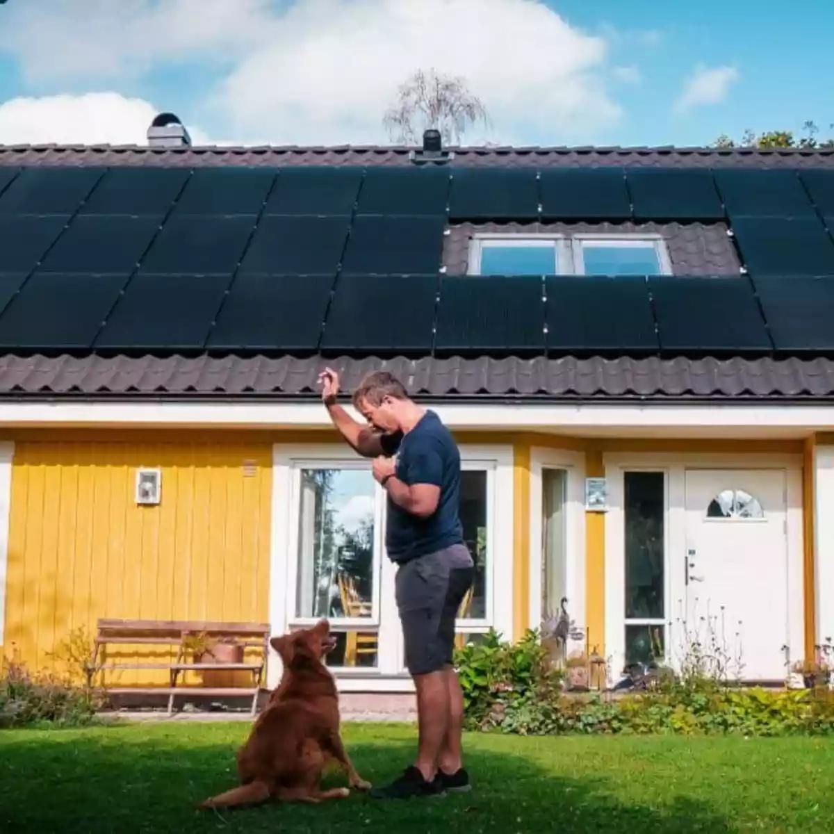 homme et son chien se tenant devant sa maison équipée de panneaux solaires