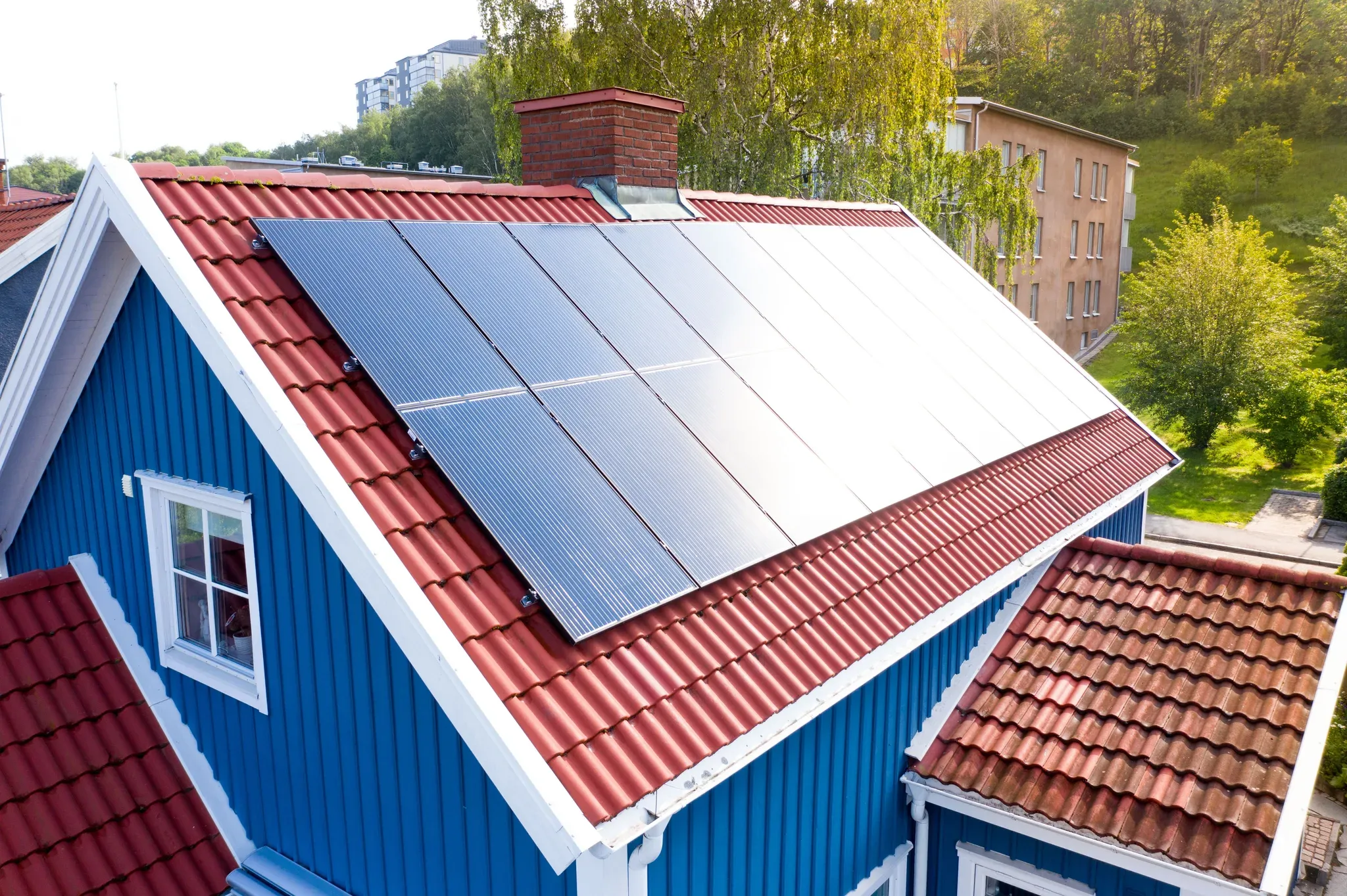 blått hus med rött tak som har solcellsinstallation